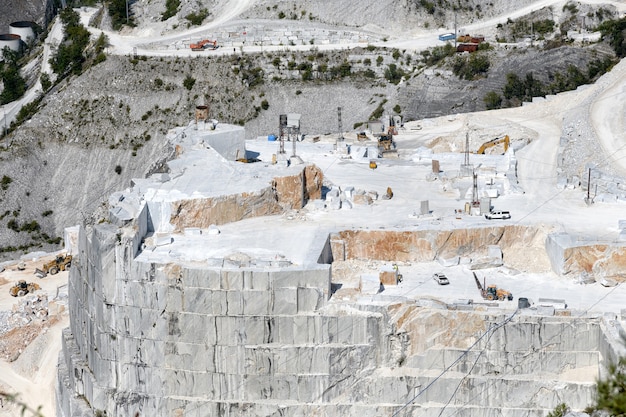 Uitzicht naar beneden in een marmeren steengroeve vallei in Carrara, Toscane, Italië met gesneden blokken steen en een terrasvormige rotswand in dagbouw