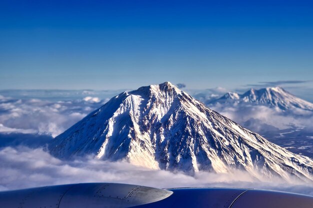 Uitzicht op de besneeuwde vulkaan vanuit de vliegtuigverlichting Piek slapende vulkaan boven de wolken