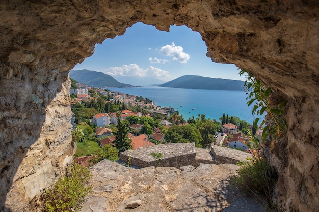 Uitzicht op de stad Herceg Novi, blauwe zee en gebouwen door het gat in de stenen muur van het fort, Montenegro. De stad gelegen bij de ingang van de prachtige baai van Kotor of de baai van Boka Kotor
