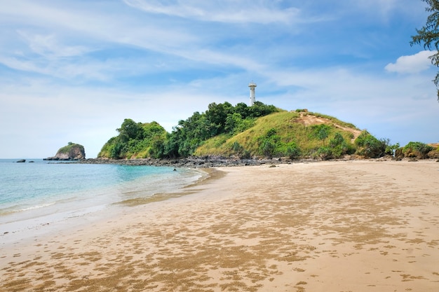 Foto uitzicht op een prachtig tropisch strand. op de achtergrond groene rotsen met een witte vuurtoren op een blauwe hemel met wolken. koh lanta, thailand.