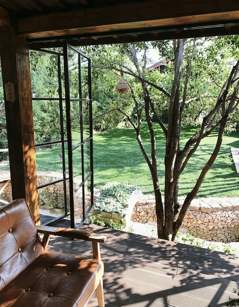 Uitzicht op een tuin vanaf een balkon met een leren stoel en een boom.
