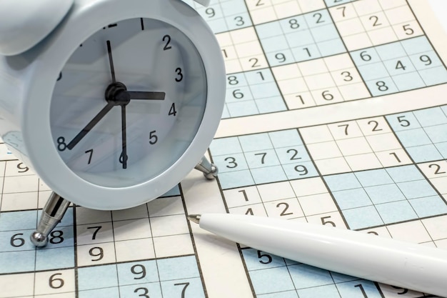 Uitzicht op een wekker en een pen op de achtergrond van een sudoku puzzel