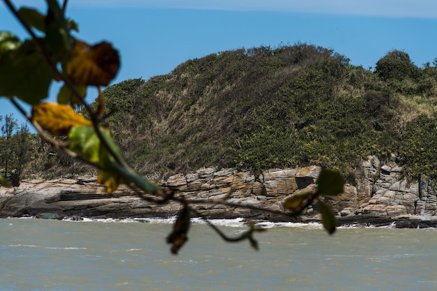 Foto uitzicht op het joana-strand in rio das ostras in rio de janeiro. zonnige dag, blauwe lucht. sterke zee en geelachtig zand en veel rotsen.