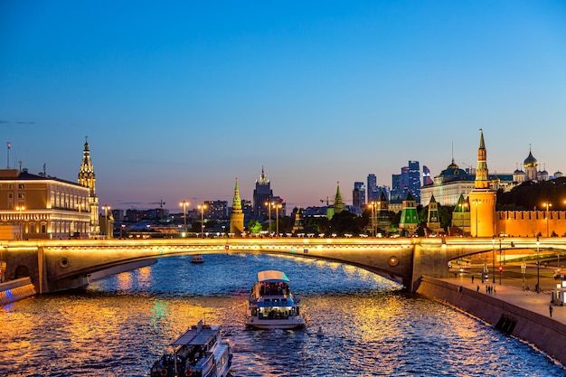 Uitzicht op het Kremlin van Moskou en de wolkenkrabbers van de stad Moskou langs de kade van de rivier de Moskou met sightseeing schepen tijdens de avond zonsondergang blauwe uur.