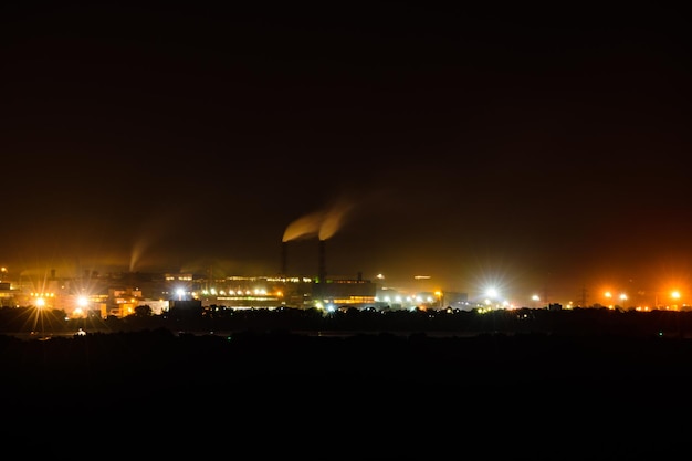 Uitzicht op stadslichten 's nachts. Rook uit schoorstenen van de fabriek stijgt naar de hemel. Milieuvervuiling concept