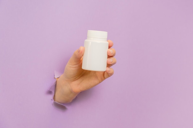 Uitzicht op witte fles plastic buis in handen op lila achtergrond Verpakking voor pillen capsules supplementen Cosmetica