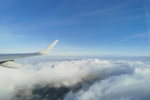 Uitzicht op witte pluizige wolken in de blauwe lucht onder de vleugel van het vliegtuig