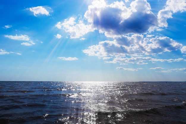 Uitzicht op zee onder blauwe lucht met wolken, zonnestralen door de wolken, mooi zonnig zeegezicht.