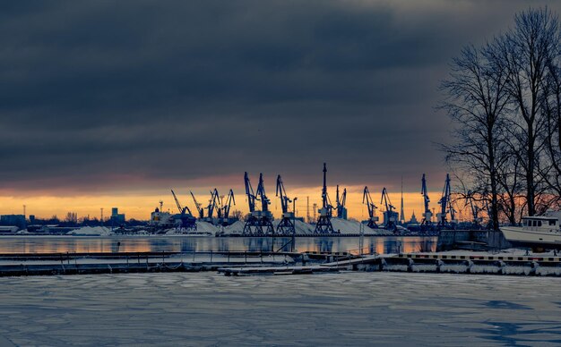 Uitzicht op zeehaven met kranen bij zonsopgang en bewolkte hemel in de winter