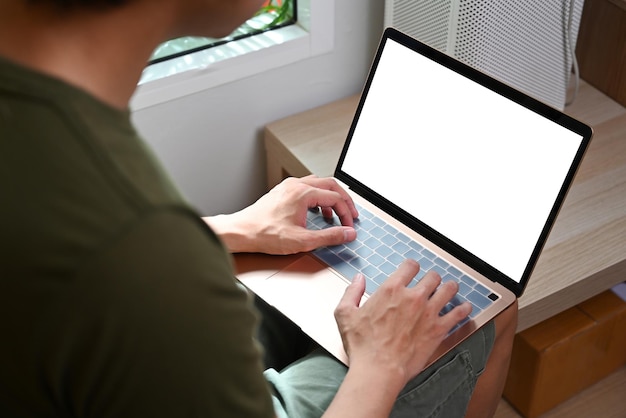 Uitzicht over de schouder van een jonge man met behulp van laptop terwijl hij in de woonkamer zit