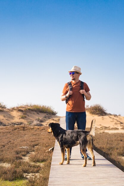 Uitzicht van achteren op een man die met zijn hond loopt op een weg die door een prachtig landschap leidt.