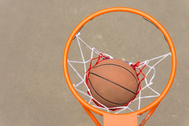 Uitzicht van bovenaf op een basketbal die door de hoepel en het net gaat op een asfaltveld buiten