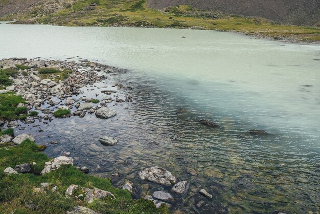 Foto uitzicht vanaf boven naar turquoise bergmeer met transparant water. sfeervol berglandschap met turquoise wateroppervlak van gletsjermeer onder stenen en gras. uitzicht van bovenaf naar hooglandmeer.