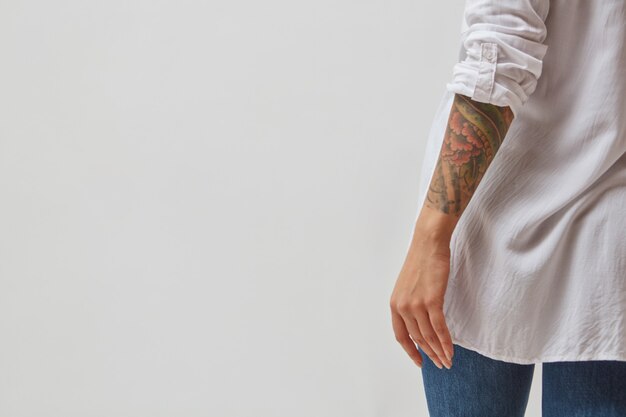 Foto uitzicht vanaf de achterkant van een meisje in jeans, een wit overhemd en met een tatoeage op haar handen op een grijze achtergrond. ruimte kopiëren