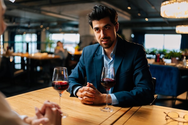 Uitzicht vanaf de achterkant van onherkenbare jonge vrouw naar glimlachende elegante man in pak zittend aan tafel met glazen rode wijn feestelijk diner in luxe restaurant