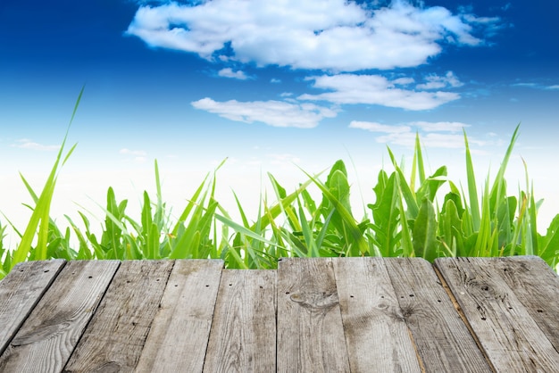 Uitzicht vanaf de lege houten dektafel naar het groene de lentegras en de blauwe hemel met wolken op de achtergrond