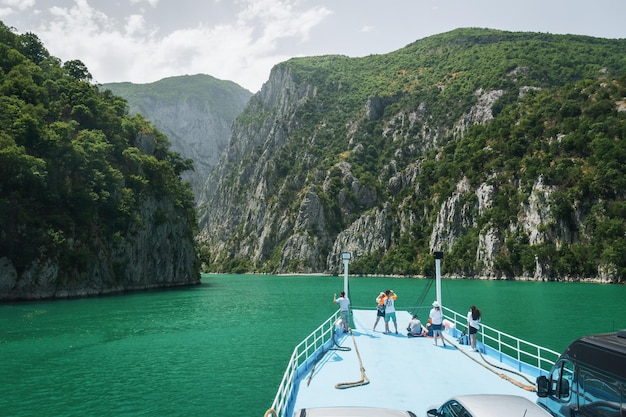 Uitzicht vanaf de veerboot op het Komani-meer Een toeristenboot haalt de autoveerboot op het Komani-meer in de dinarische Alpen in