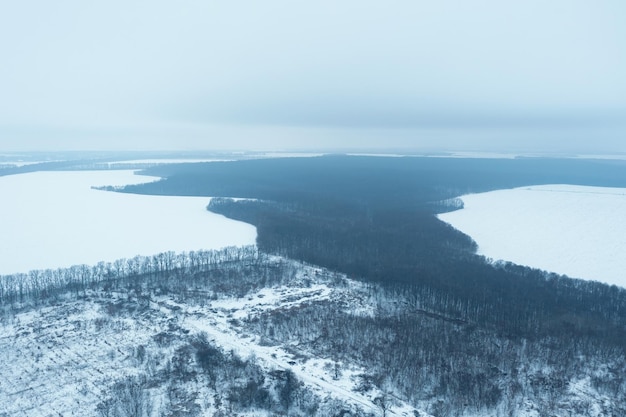 Uitzicht vanaf een hoogte op een winterlandschap met een besneeuwd veldbos en mist