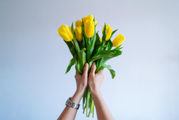 Uitzicht vanuit de eerste persoon. vrouw houdt boeket gele tulpen vast. witte achtergrond