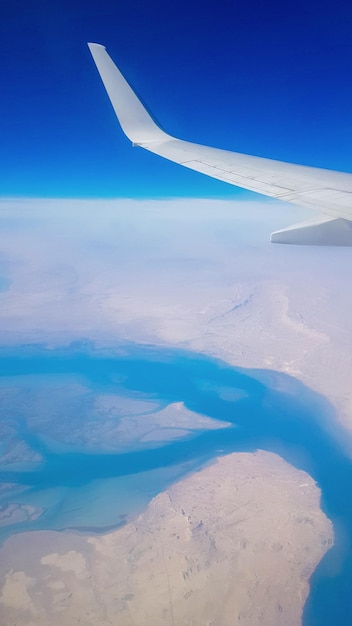 Uitzicht vanuit het raam van het vliegtuig op de blauwe lucht en aarde met landschap van woestijnzee en kanalen in Emiraten