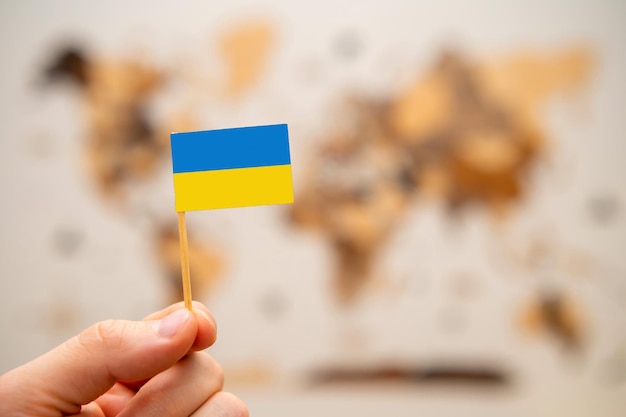 世界地図の背景に男の手でウクライナの旗