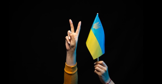 Ukraine national flag on a stick in hands Symbol of Ukrainian statehood Hand gesture V sign for victory or peace in Ukraine Copy space