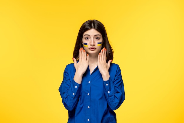 Ukraine russian conflict brunette pretty cute girl with flags on cheeks with hands up scared