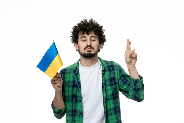 Ukraine russian conflict cute young brunette guy green shirt and ukrainian flag crossing fingers