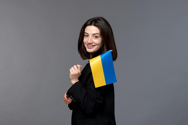 Ukraine russian conflict dark hair cute young woman in blazer holding ukrainian flag smiling