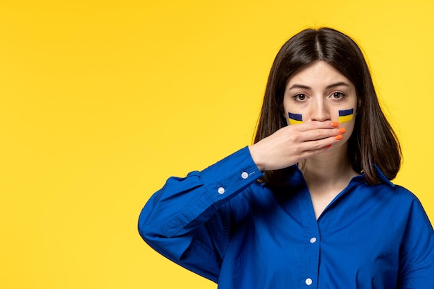 Ucraina conflitto russo giovane bella ragazza bandiere sulle guance sfondo giallo che copre la bocca Foto Premium
