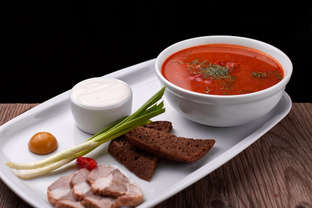 Ukrainian borsch with sour cream, onions and bacon on a white plate