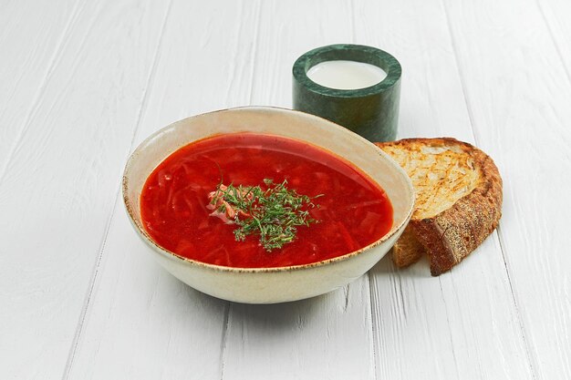 Ukrainian borscht with sour cream in a plate on a white wooden background