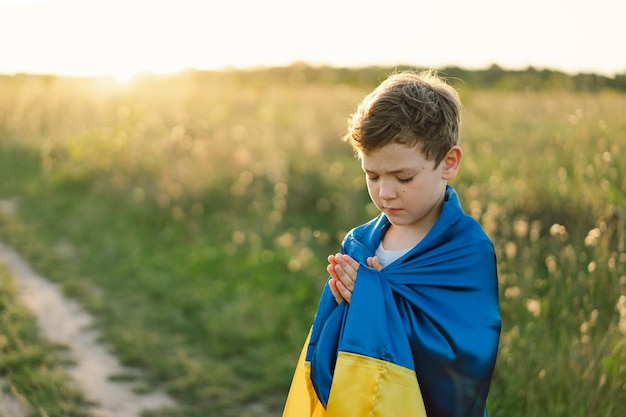 Ukrainian boy closed her eyes and praying to stop the war in Ukraine in a field at sunset Hands folded in prayer concept for faith spirituality and religion War of Russia against Ukraine Stop War