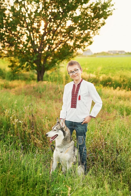 Ragazzo ucraino bambino con cane husky in un campo in estate al tramonto