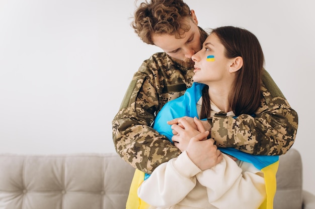 Ukrainian couple military man in uniform hugs and wraps his wife in the Ukrainian flag The concept of patriotism