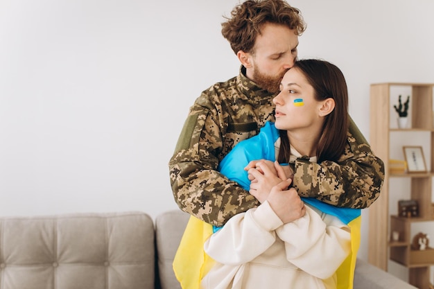 Ukrainian couple military man in uniform hugs and wraps his wife in the Ukrainian flag The concept of patriotism