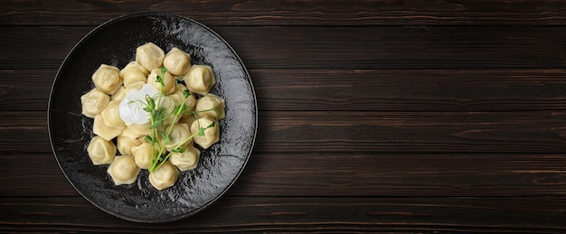 Ukrainian dumplings with sour cream and microgreen on a black glossy plate on a wooden background