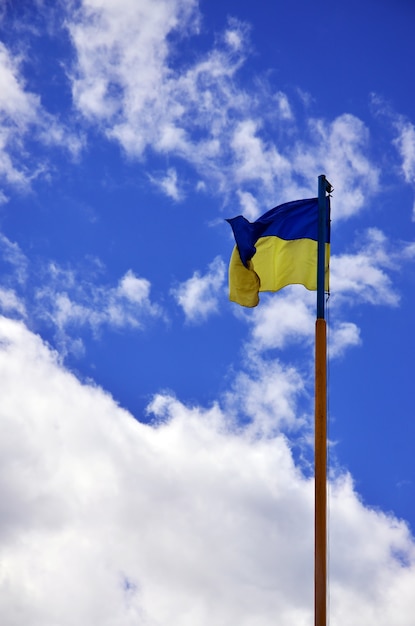 Ukrainian flag against the blue sky with clouds. 