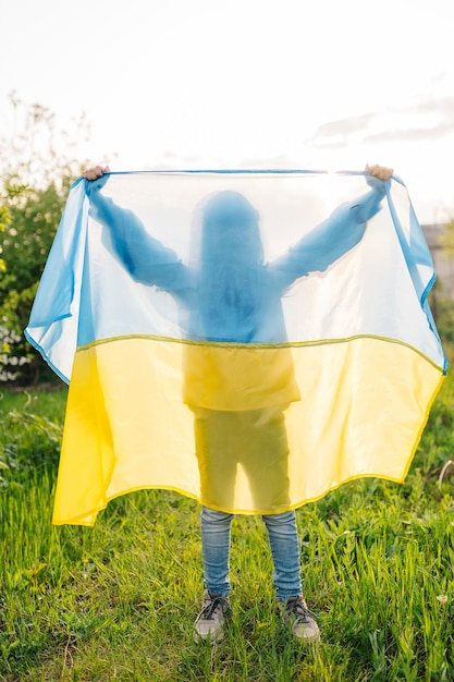 Foto bandiera ucraina e silhouette bambino silhouette di un bambino dietro una bandiera ucraina illuminata dal sole pomeridiano in un ritratto blu e giallo