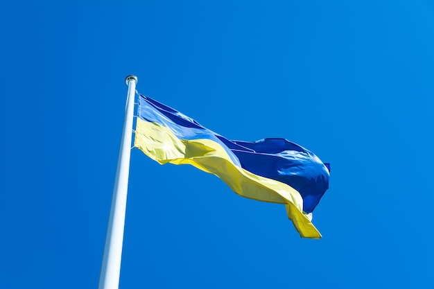 Ukrainian flag on flagpole waving on the wind against blue sky background