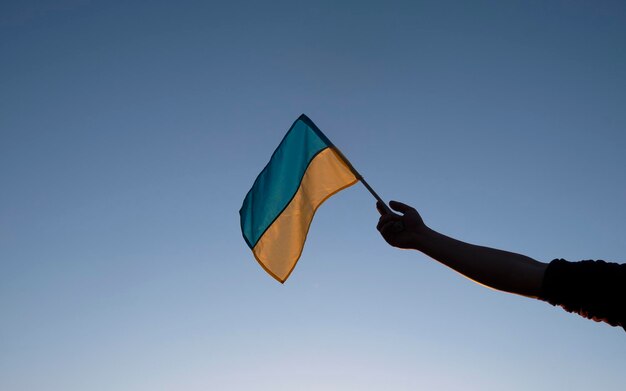 Ukrainian flag in hand over clear blue sky