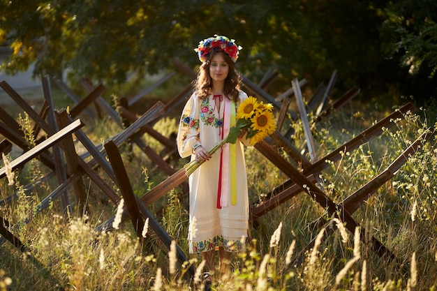 A Ukrainian girl in a Ukrainian national vyshyvanka dress with a bouquet of sunflowers, anti-tank he