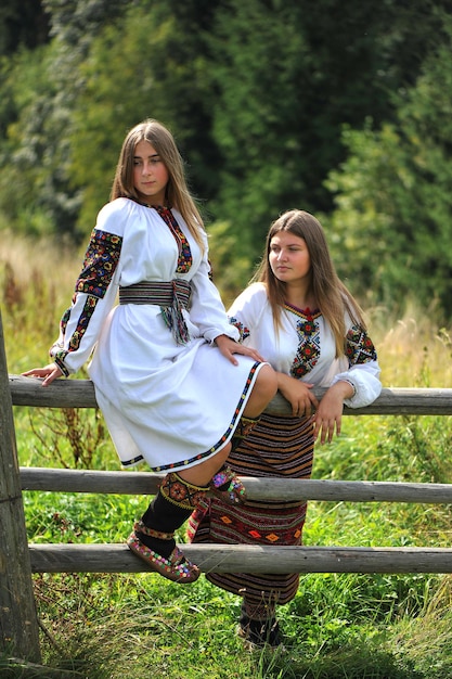 Фото Украинские девушки, одетые в национальную гуцульскую одежду, сидят на заборе.