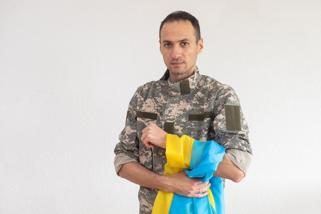 군용 픽셀 제복을 입은 우크라이나 남자 전사는 우크라이나의 노란색-파란색 깃발을 들고 사슬에 삼지창의 작은 문장을 닫습니다.