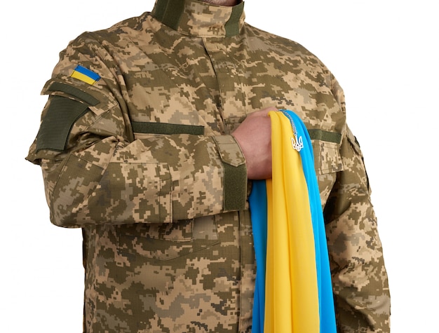 Ukrainian man warrior dressed in a military pixel uniform holds the yellow-blue flag of the state of Ukraine
