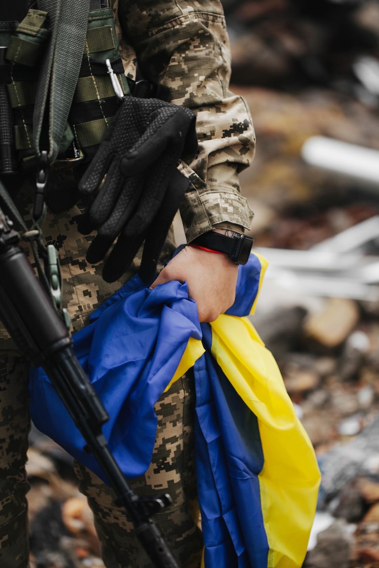 Фотография украинская военная женщина с украинским флагом в руках на фоне взорванного дома