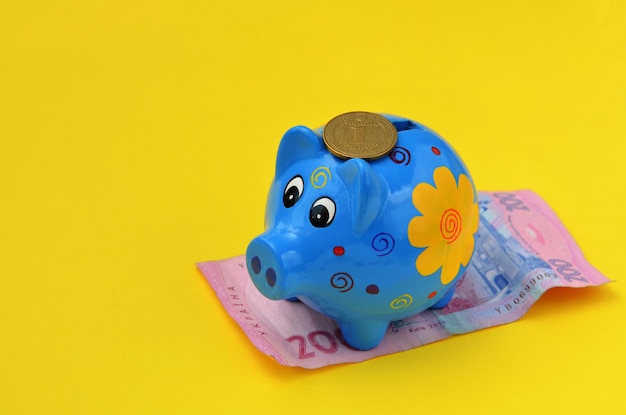 Ukrainian money and a blue piggy bank on a yellow background closeup
