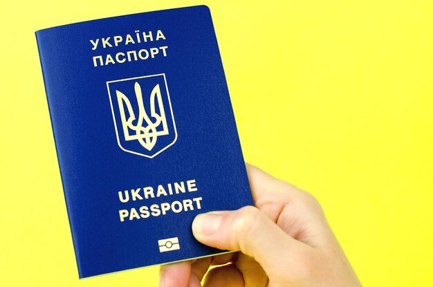 Украинский паспорт в женской руке на желтом фоне