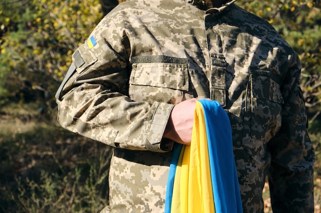 Ukrainian soldier holds in his hand the yellow-blue flag of the state, he pressed his hand to his chest