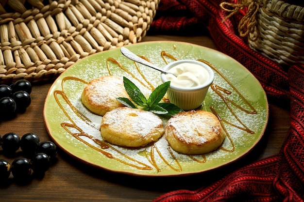 Ukrainian syrnyky with sour cream and powdered sugar in a plate tasty cottage cheese pancakes